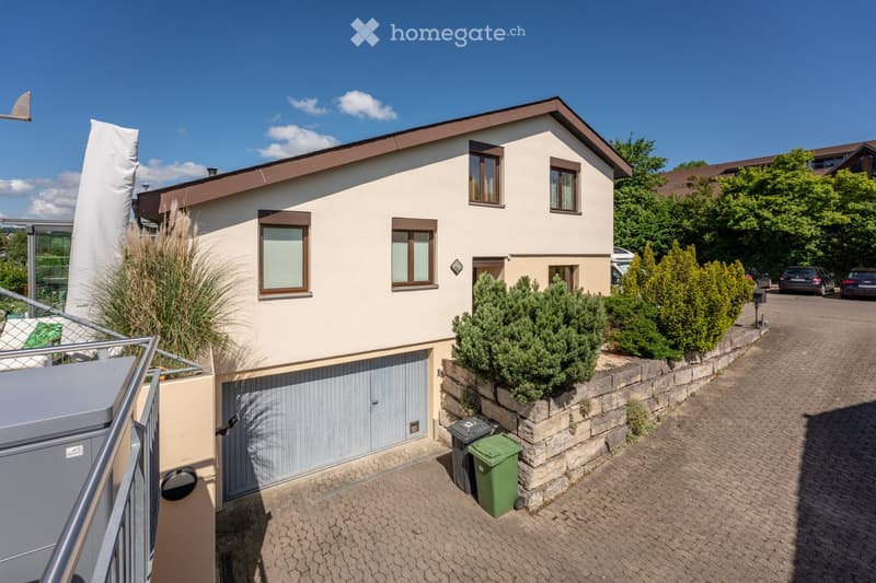 2 story house, beige exterior, brown roof, garage, brick driveway, plants, trees