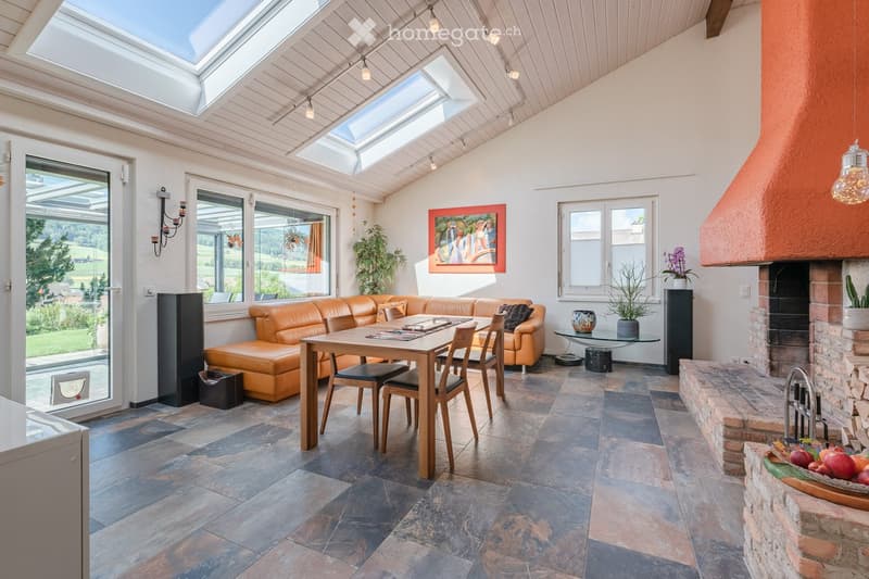dining room with fireplace, skylights, large windows, orange leather sofa, wooden dining table, wooden chairs, plants, picture frame