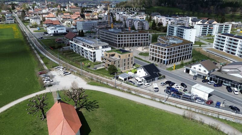Aerial view of a town with multiple buildings, some under construction, green spaces, and a railway track.