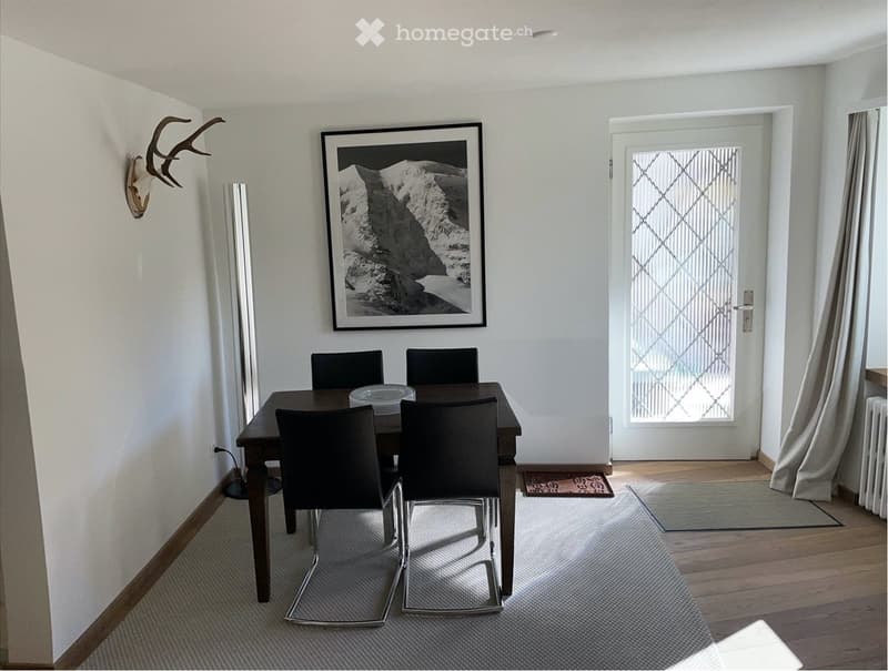 Dining room with a wooden table, black chairs, a picture frame on the wall, a radiator, and a glass door.