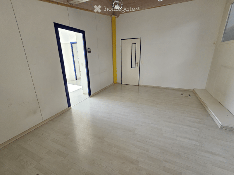 empty room, white walls, wooden floor, two doors, one with blue trim, yellow pipe