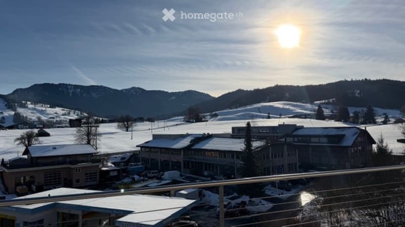 Building with snow on the roof, surrounded by snow-covered mountains, clear sky, sun shining