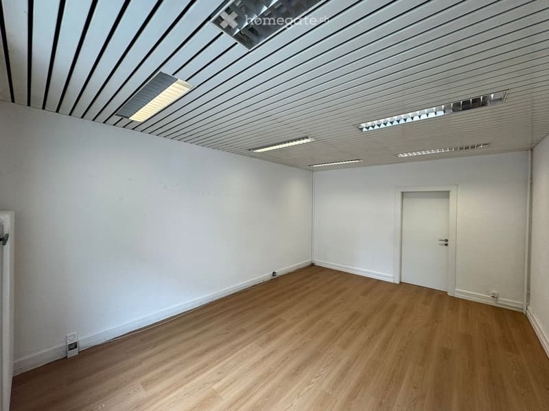 An empty room with white walls, wooden floors, and a ceiling with recessed lighting.