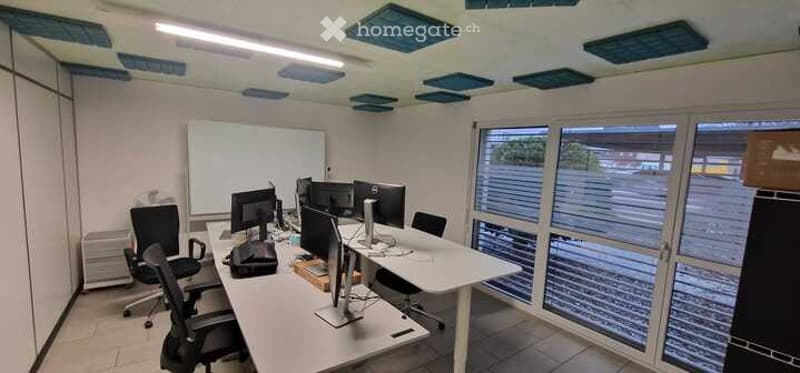office room with white desk, black chairs, computer monitors, whiteboard, glass windows