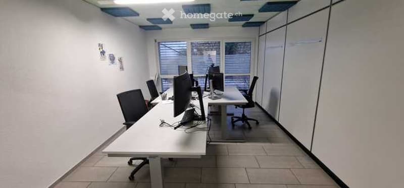 Office room with white walls, tiled floor, desks, chairs, computer monitors, windows with blinds