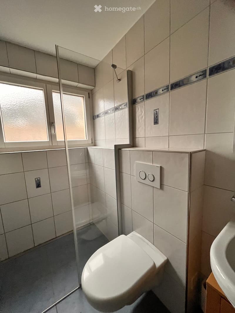 Bathroom with white tiles, glass shower enclosure, white toilet, white sink, window
