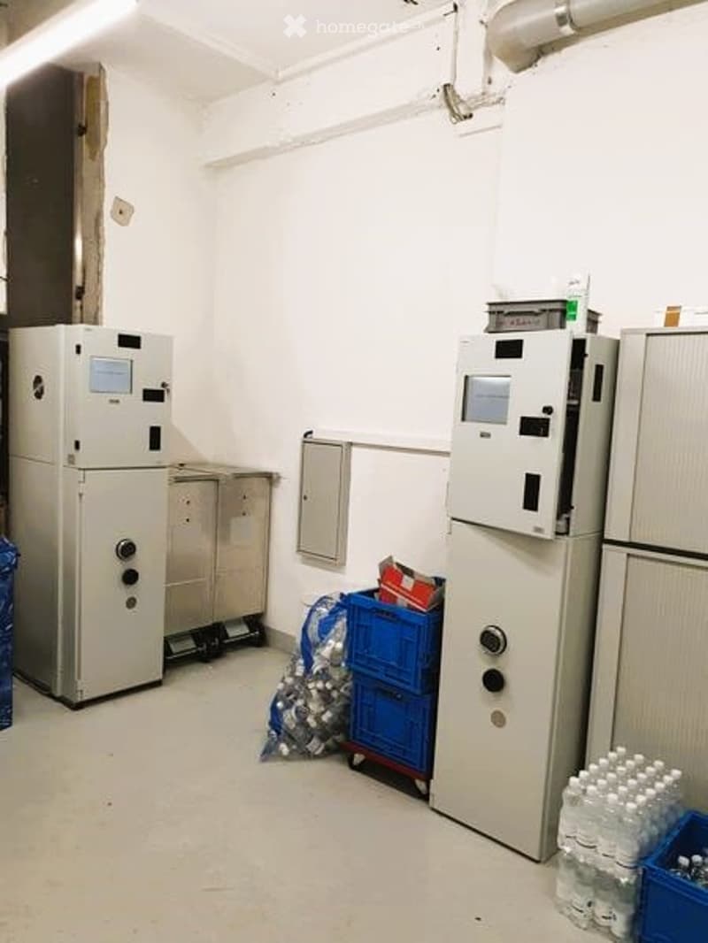 A room with white walls, white floor, two large white machines, a blue crate, a silver cabinet, and a blue plastic bag