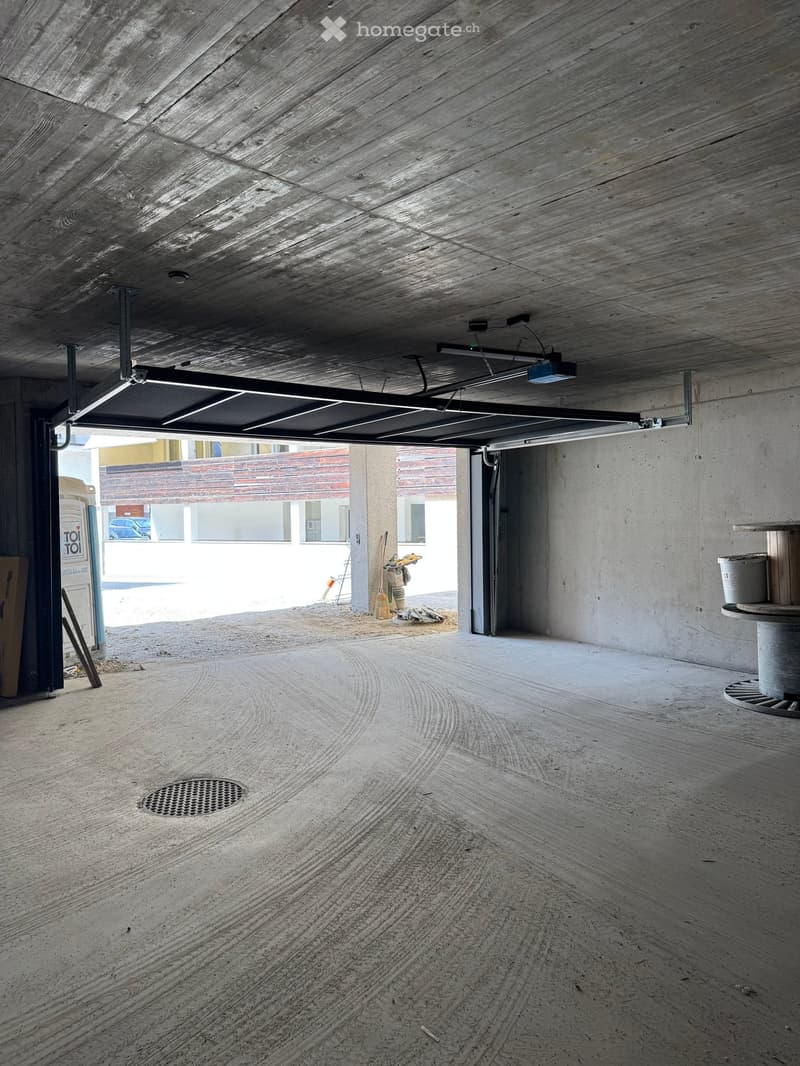 Empty garage with concrete ceiling, open garage door, and a drain in the floor