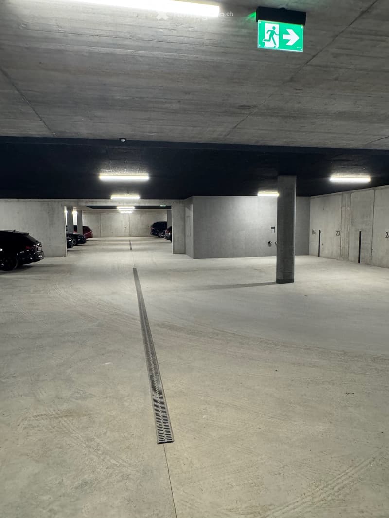 underground parking lot, concrete floor, white markings, emergency exit sign, cars parked