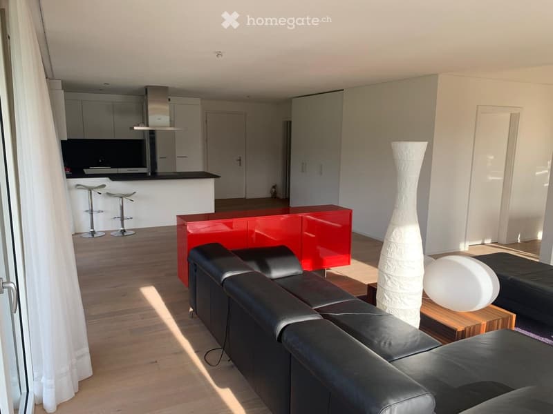 modern living room with black leather sofa, red cabinet, white curtains, wooden floor, white walls, kitchen with black countertops, white cabinets, and stools