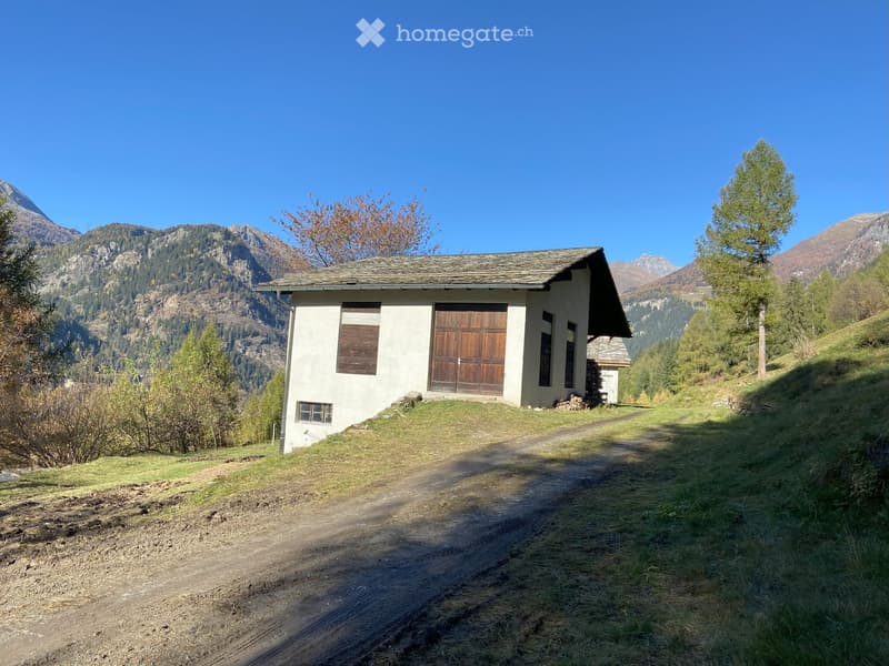 Small house with wooden garage, located on a hillside with mountain views