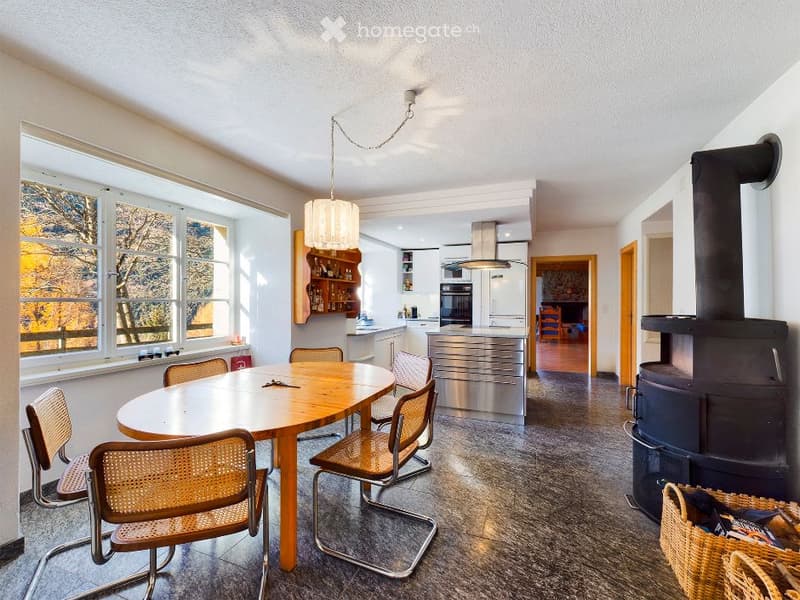 Dining room with wooden table, chairs, fireplace, large windows, kitchen with modern appliances
