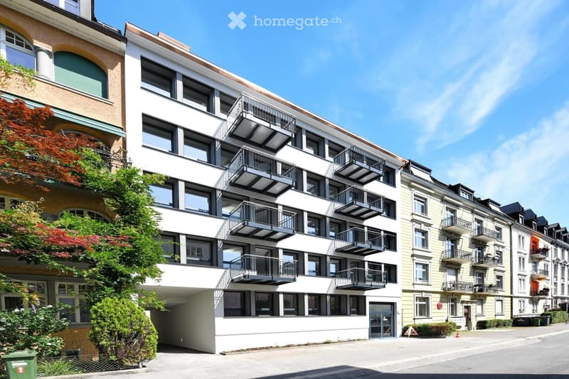 Modern apartment building with multiple balconies, white exterior, multiple floors, and a driveway.