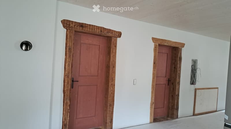 An empty room with two wooden framed doors and white walls. There is a light switch on the wall between the doors.