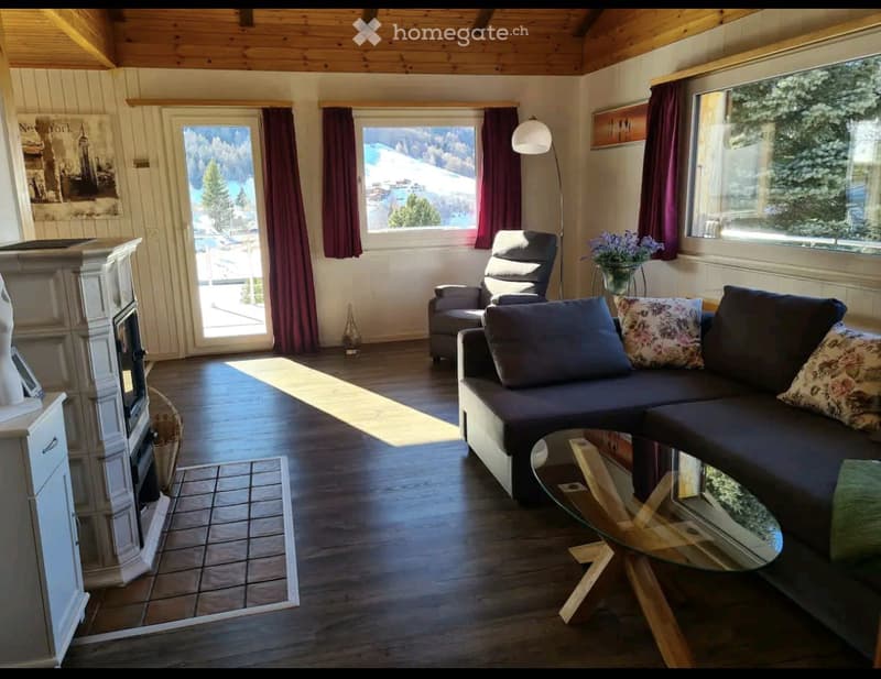 Living room with fireplace, large windows, wooden floor, couch, coffee table, armchair, and a view of the mountains