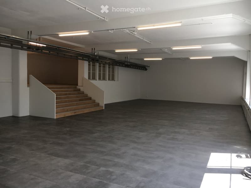 empty room, gray floor, white walls, wooden staircase, fluorescent ceiling lights