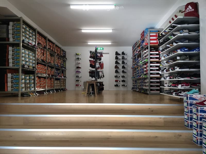 shoe store with wooden floor, white walls, shelves with shoes, boxes of shoes, table with clothes