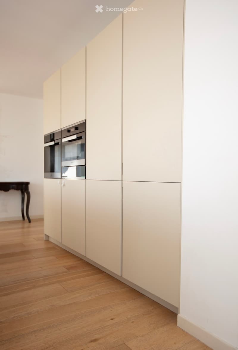 modern kitchen with white cabinets, wooden floor, two built-in ovens, wooden table