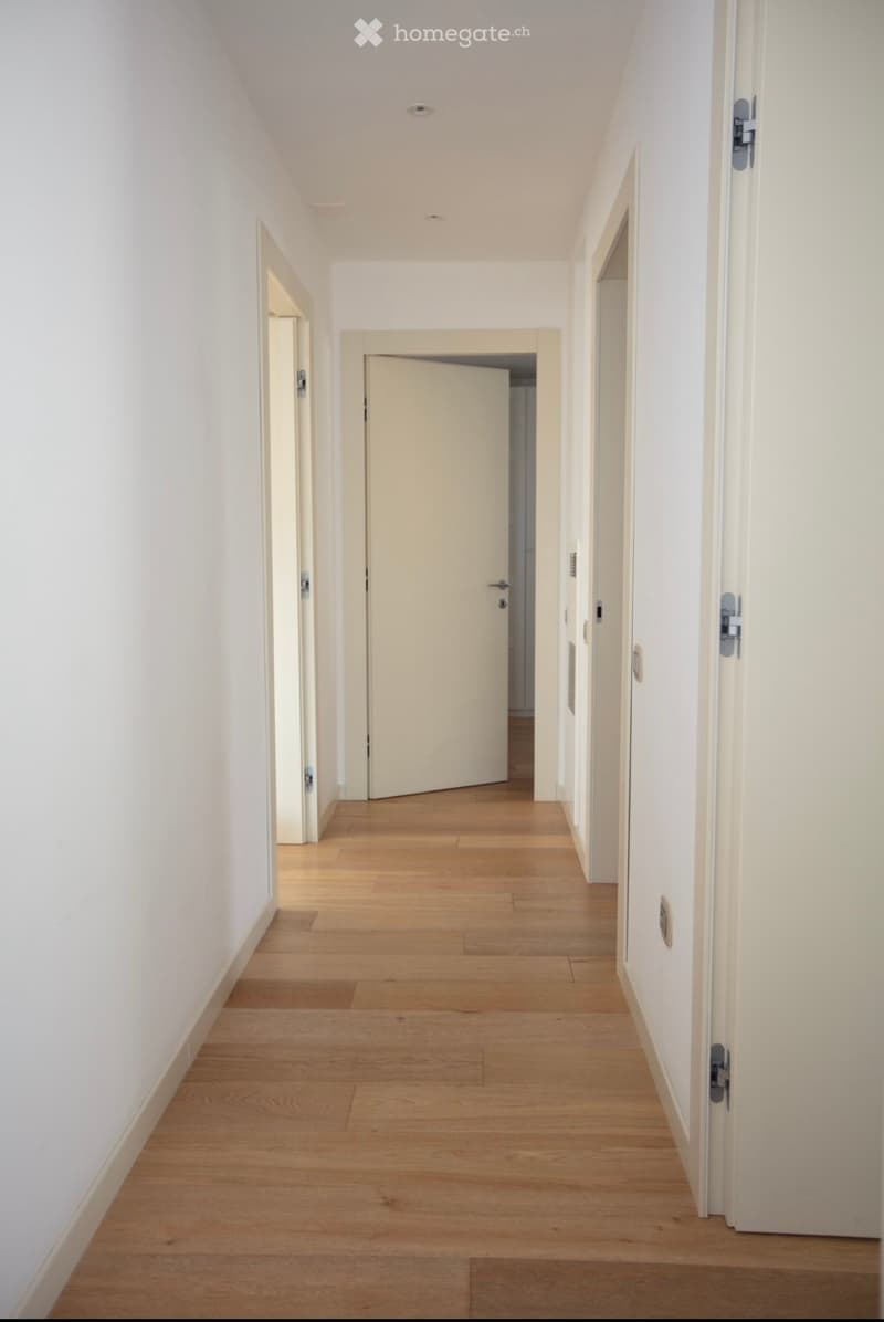 Empty hallway with wooden floor and white walls, doors on both sides