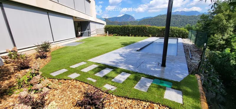 Well-maintained garden with artificial grass, stepping stones, gravel border, and modern house in the background.