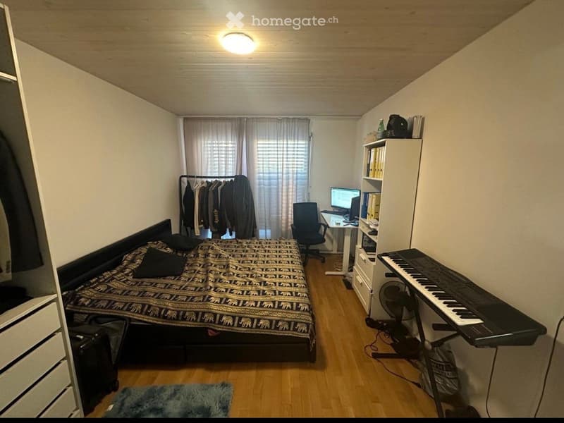 Bedroom with bed, desk, chair, piano, wardrobe, rug, and clothes hanging on a rack