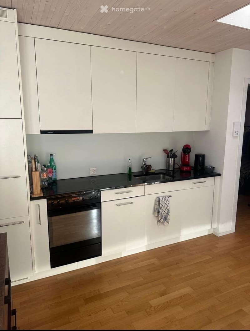 modern kitchen with white cabinets, black countertops, stainless steel appliances, wooden floor
