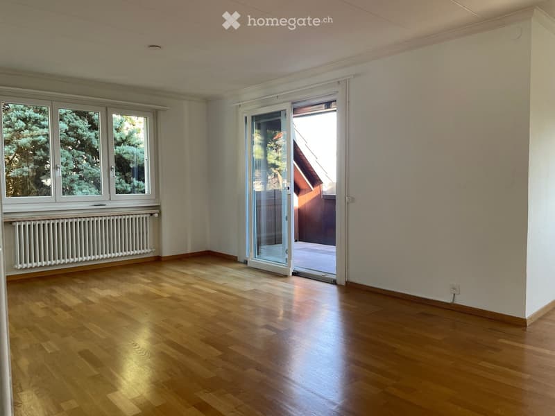 Empty room with wooden flooring, large windows, and a sliding glass door leading to a balcony or outdoor area.