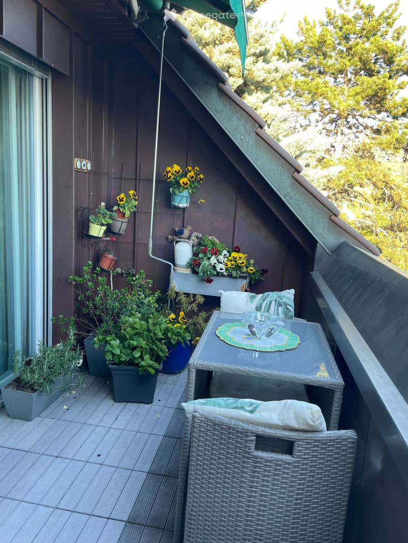 Balcony with wooden floor, table, chairs, plants, flowers, and a view of the trees