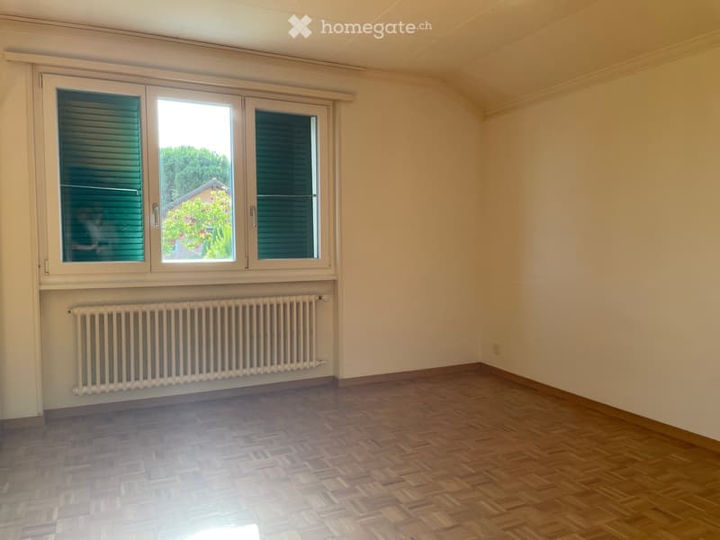 Empty room with wooden flooring, white walls, large window with shutters, and a radiator below the window.