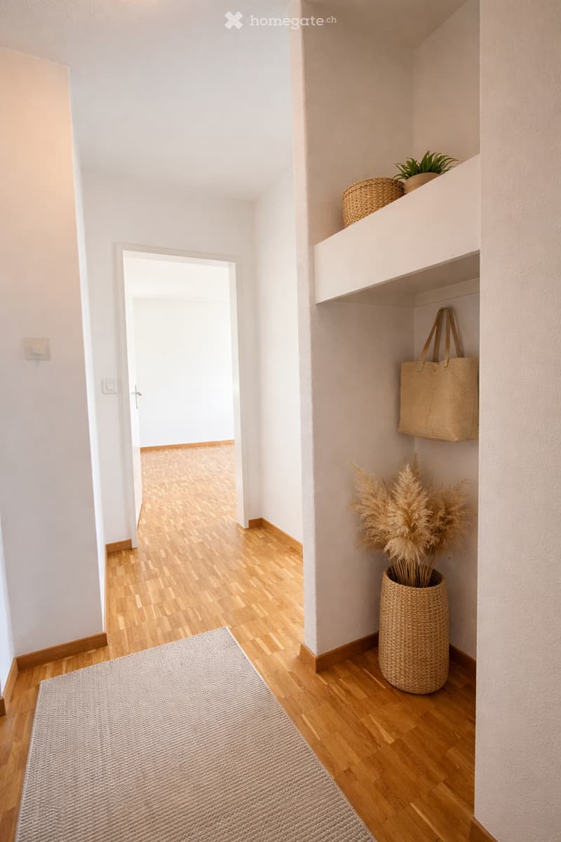 Empty hallway with wooden floor, white walls, rug, and decorative items
