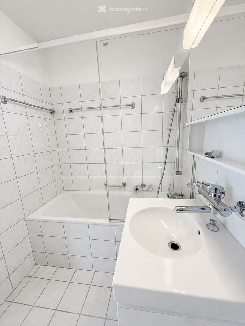 white tiled walls, white bathtub, white sink, glass shower enclosure, white shelves