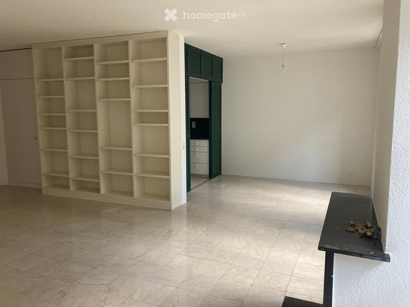 Empty room with white walls, tiled floor, large white shelf, black table, green door, white cabinet