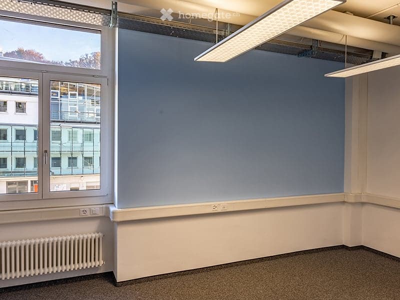 Empty room with white walls, blue wall, large window, radiator, ceiling lights