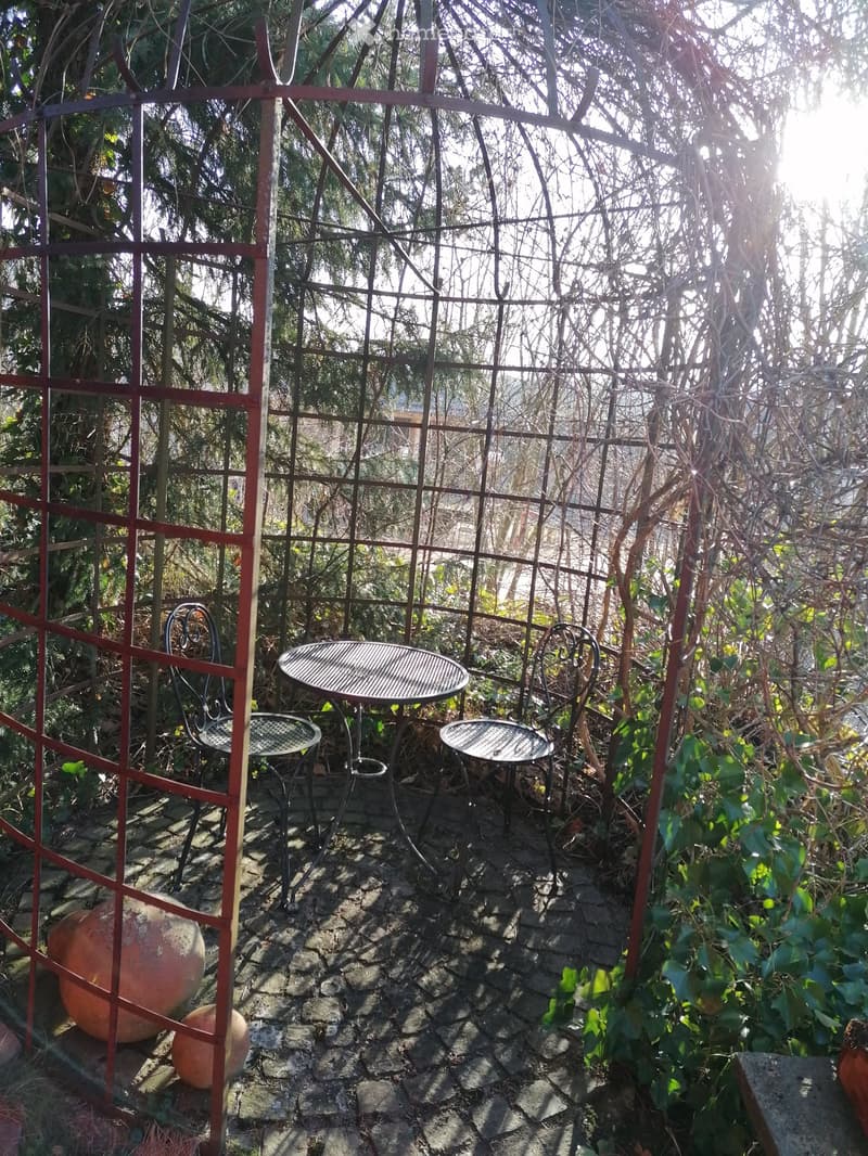A garden with a metal gazebo, a table and chairs, and a view of the surrounding area.