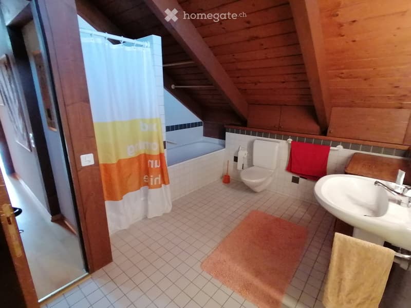 Bathroom with wooden ceiling, bathtub, toilet, sink, shower curtain, towels, and a rug