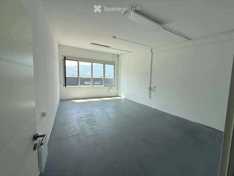 Empty room with white walls, concrete floor, and large windows offering a view of mountains.