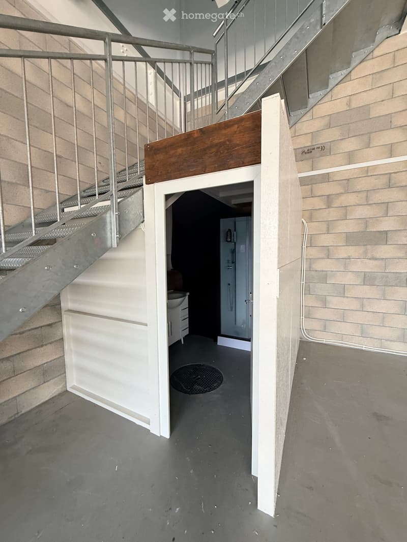 Modern hallway with a metal staircase, white walls, and a small bathroom visible at the end.