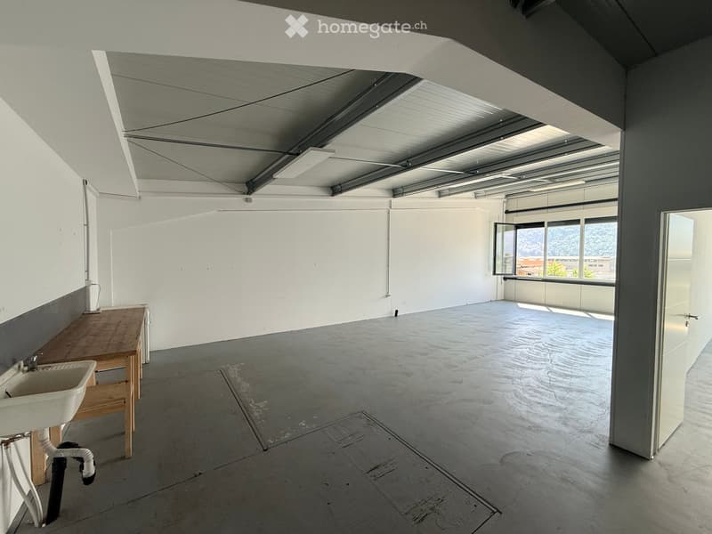 Minimalist room with concrete floor, white walls, a sink, and a wooden bench. Large windows provide natural light and a view of the outside.