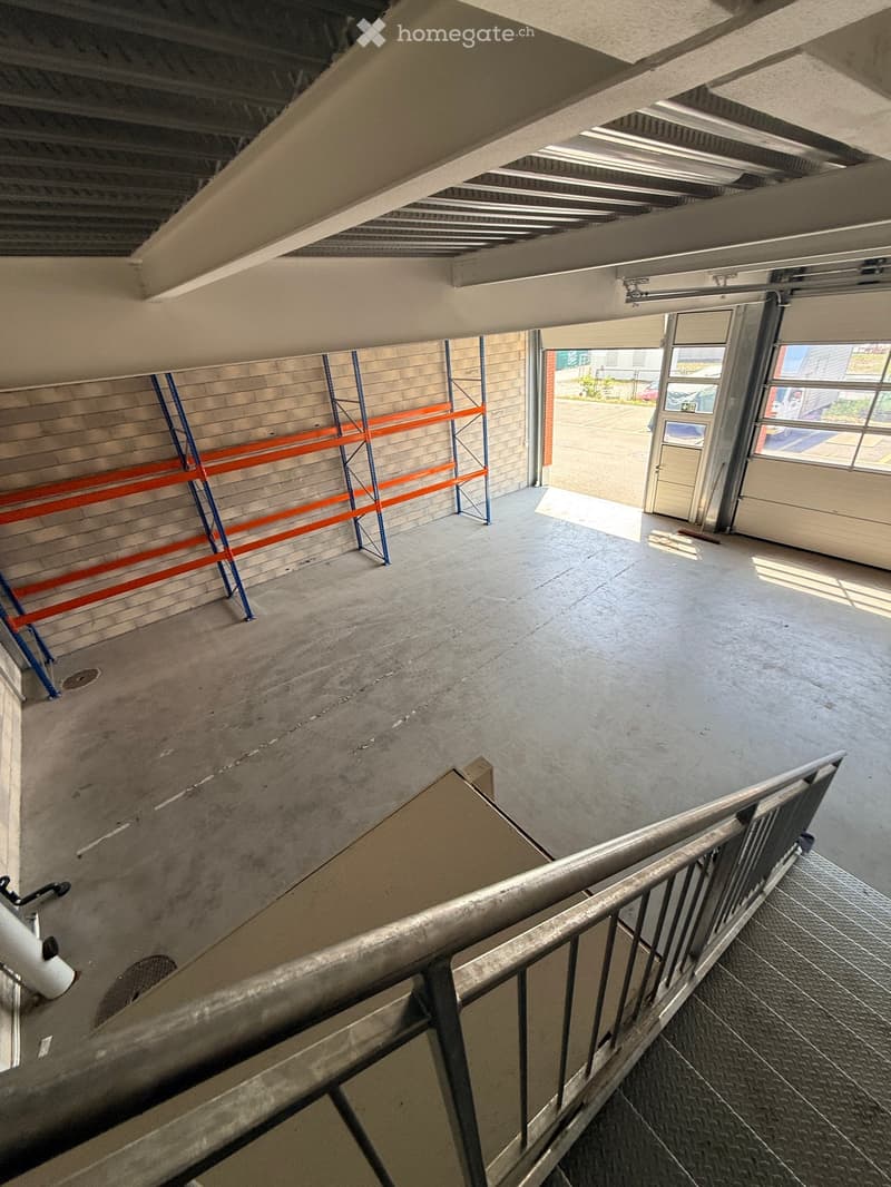 Empty concrete corridor with metal staircase, scaffolding, and a partially open door leading outside.