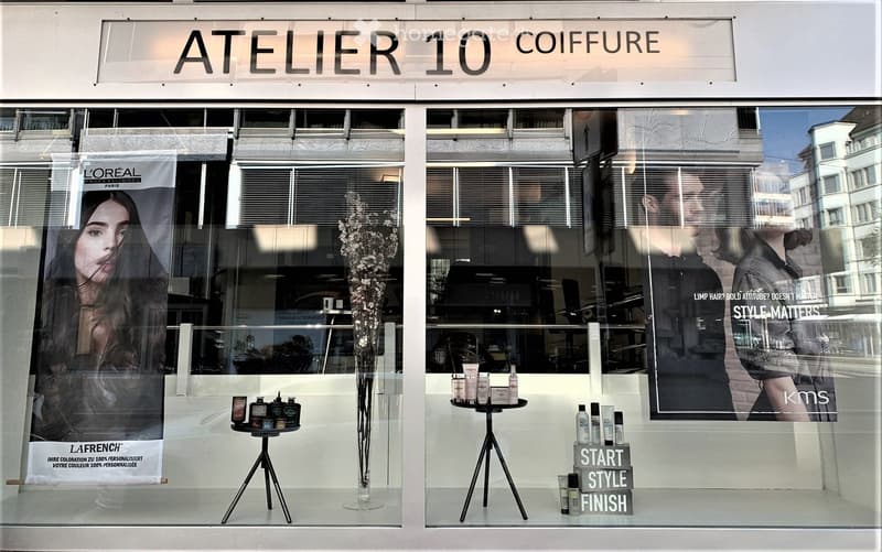 Hairdresser shop front with glass walls and windows, promotional advertisements, interior displays of beauty products, a logo on the top