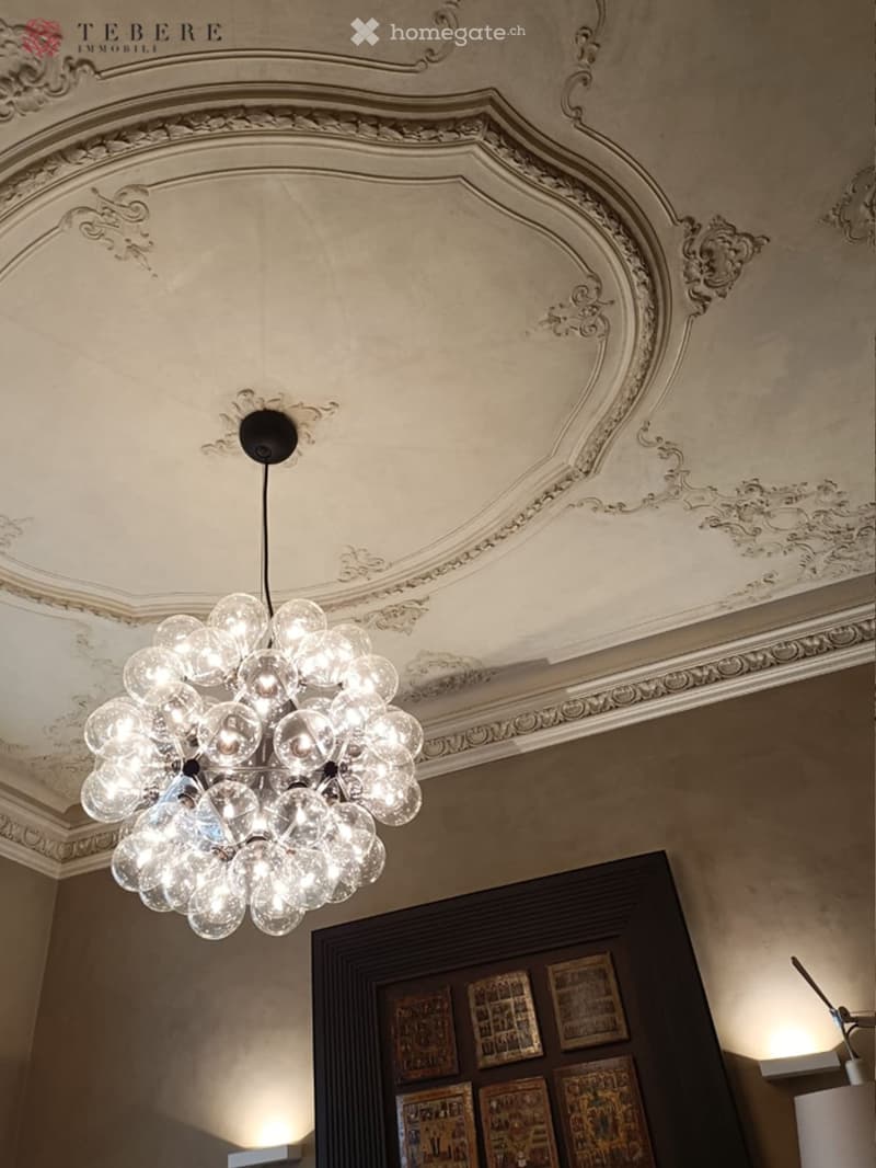 A room with a large chandelier, a wooden door, and a wall with a series of framed pictures.