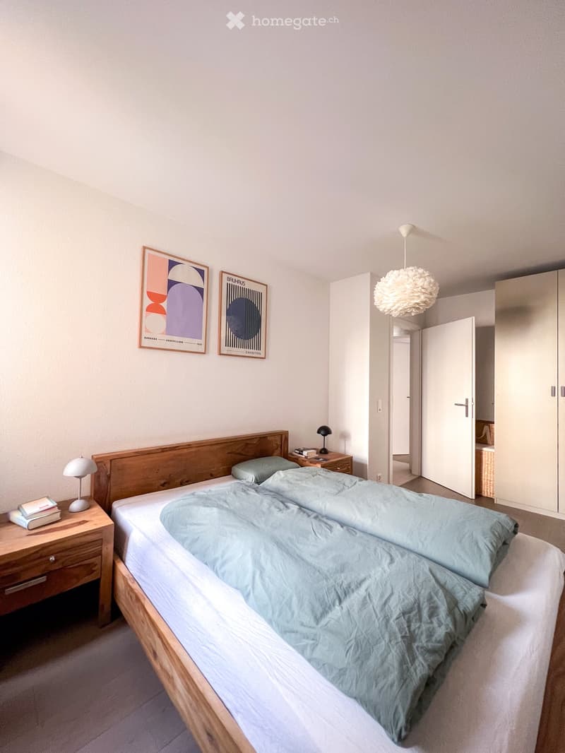 Bedroom with two beds, wooden nightstands, lamps, framed art, white walls, wooden floor, white ceiling, open door, closet, chandelier