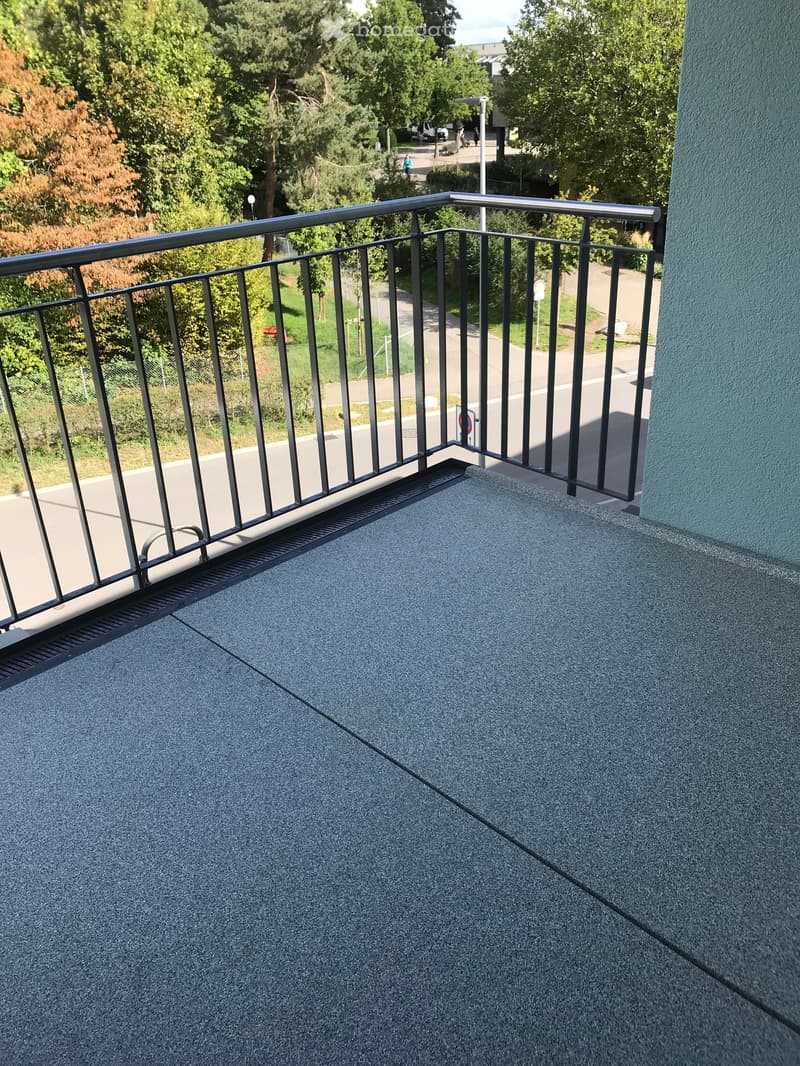 Balcony with metal railing, paved floor, view of a road and trees
