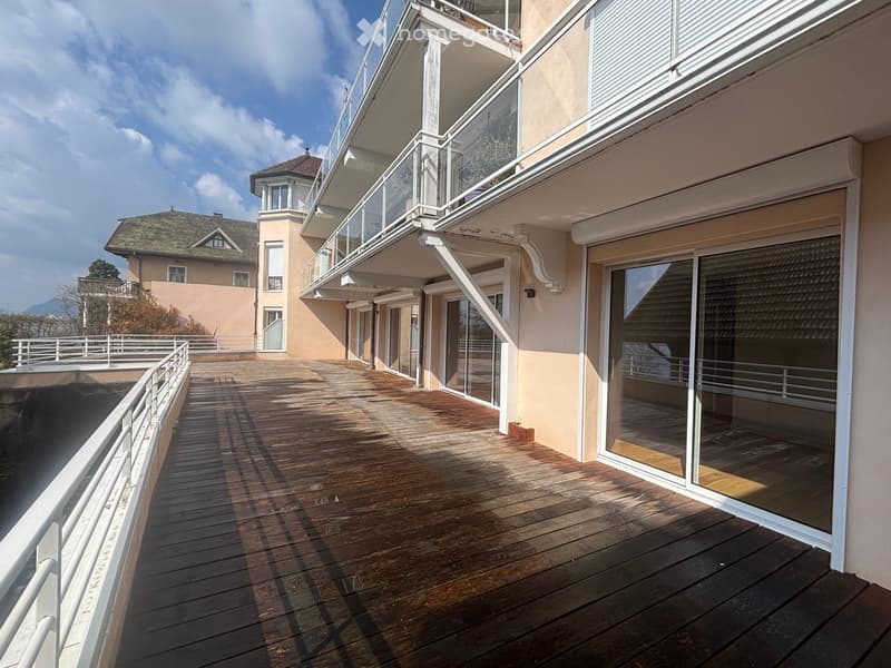 Building with wooden deck, balconies, glass doors, white railings, beige walls, and a neighboring house