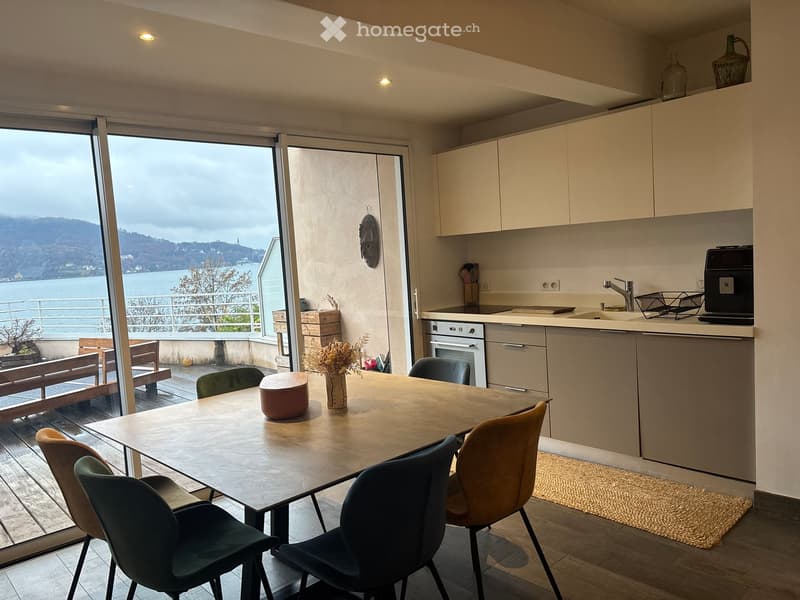 Dining area with a table and chairs, kitchen with appliances, sliding glass doors to a balcony, wooden floor, large windows