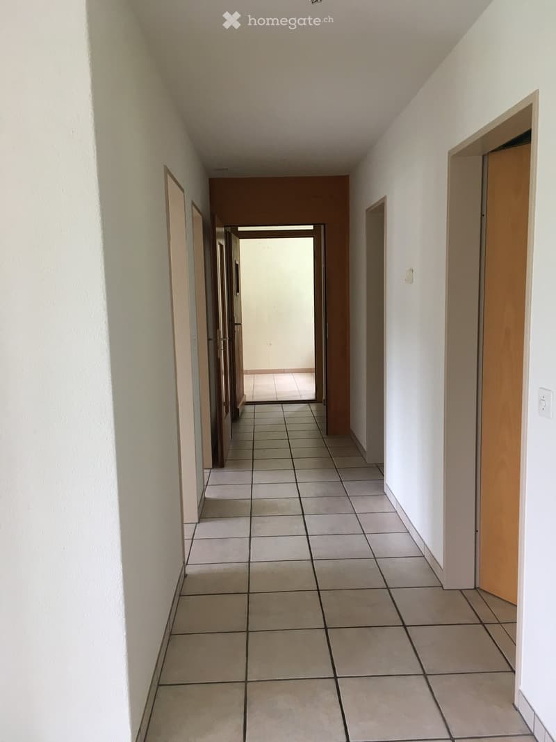 Empty hallway with tiled floor, white walls, wooden doors, and a power outlet on the right wall.