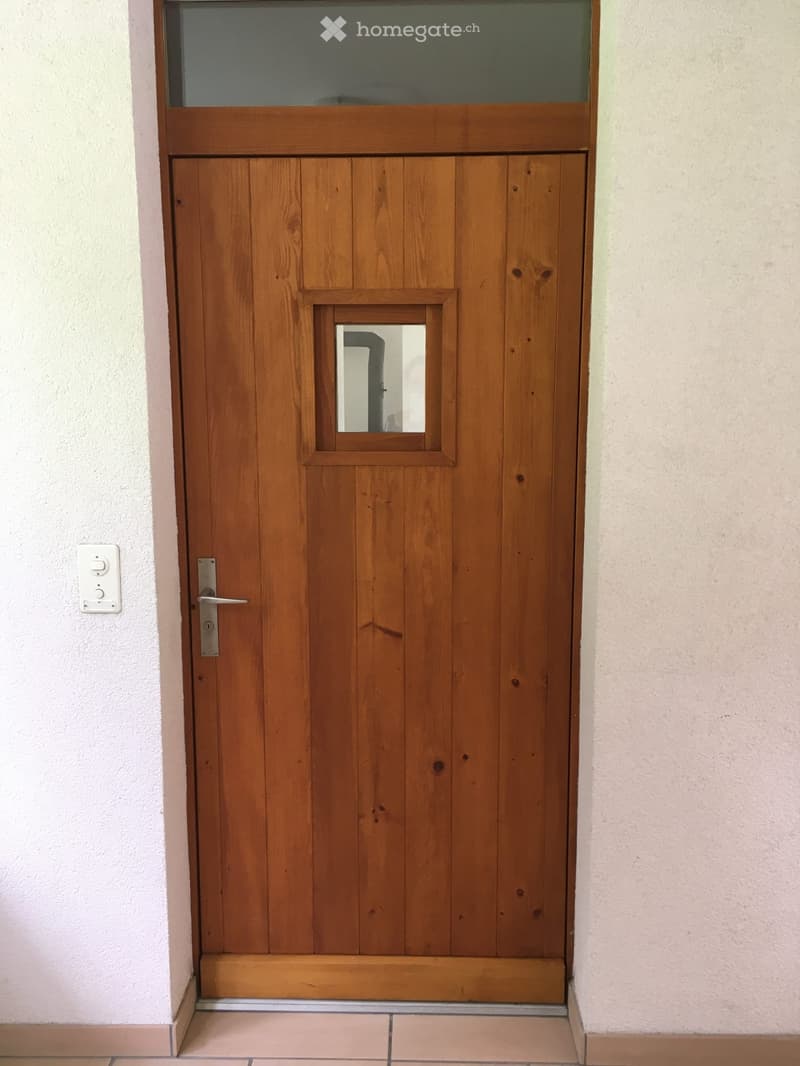 wooden door with glass window, silver handle, white switch on the wall