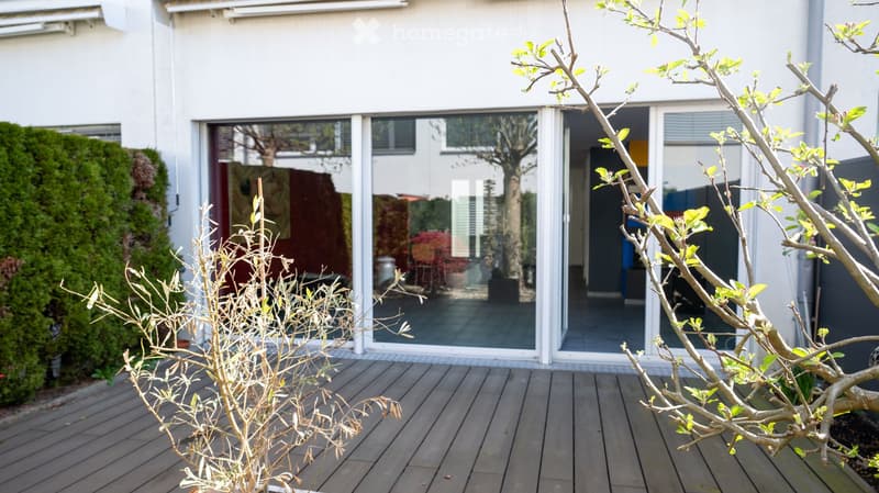 white house, large glass sliding doors, wooden deck, shrubs, trees