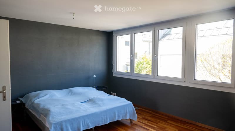 bedroom with bed, bedside table, lamp, large windows, wooden floor, gray walls