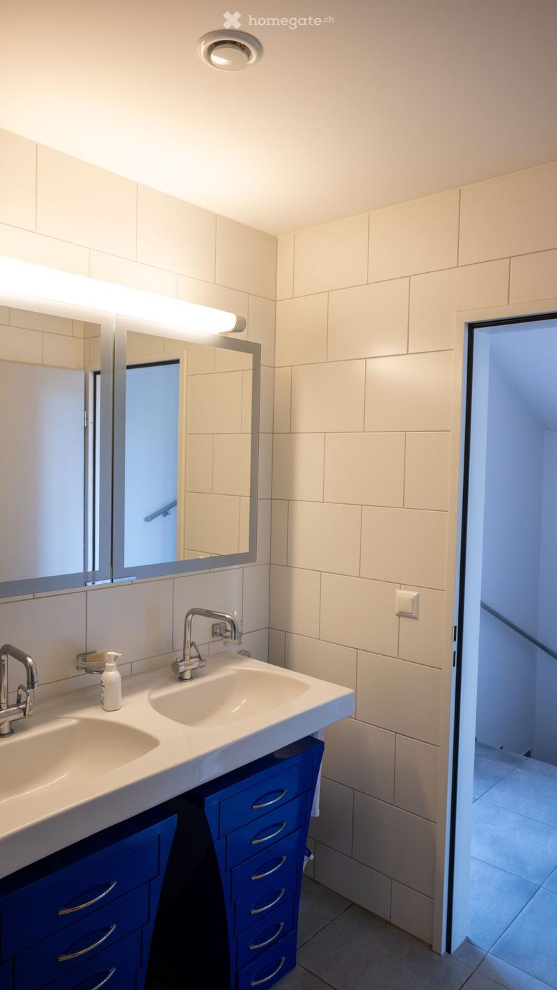 Bathroom with two sinks, blue cabinets, white tiles, mirror, and a light above the mirror.
